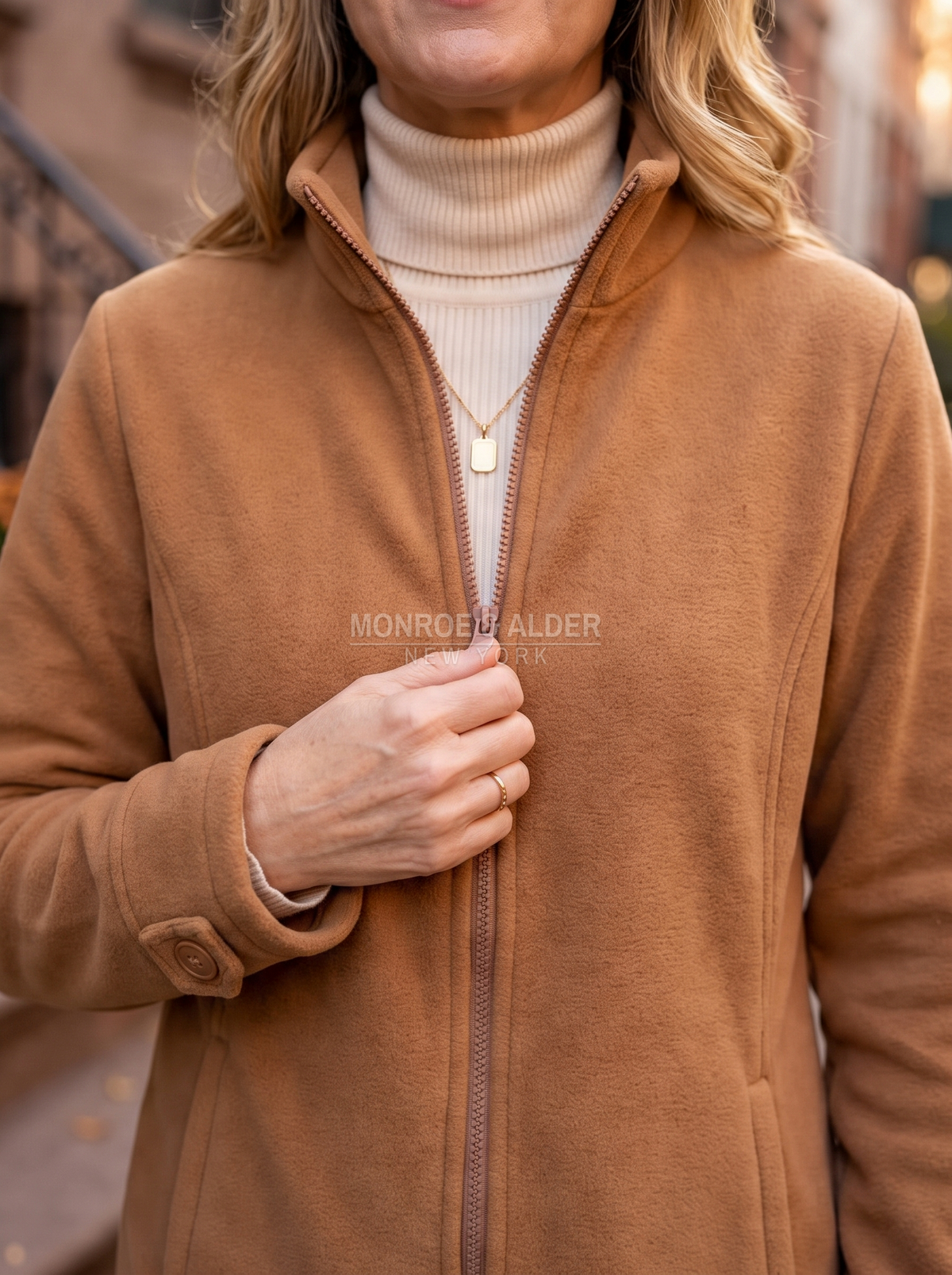 Close view of the stand collar, zipper and buttoned cuff tab in camel fleece