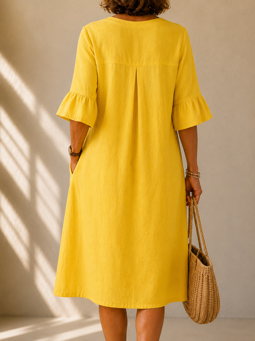 Back view of the Annette dress in Yellow, showing the box pleat and the ruffled three-quarter sleeves