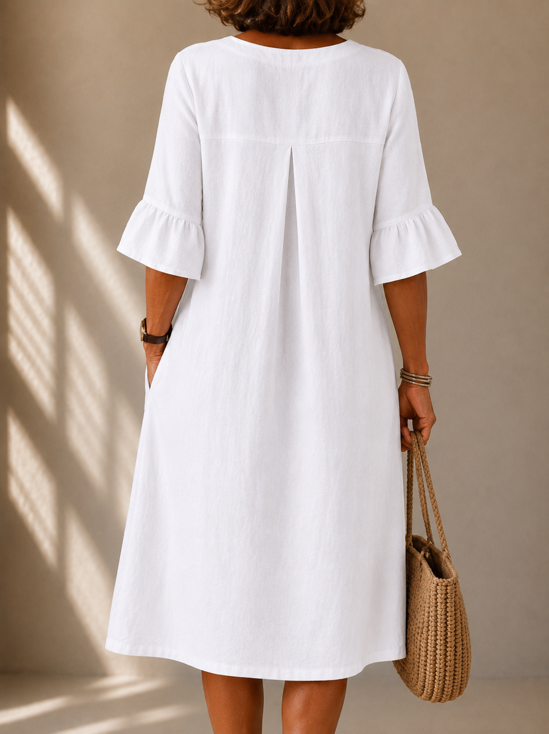 Back view of the Pearl dress in White, showing the box pleat and the ruffled three-quarter sleeves