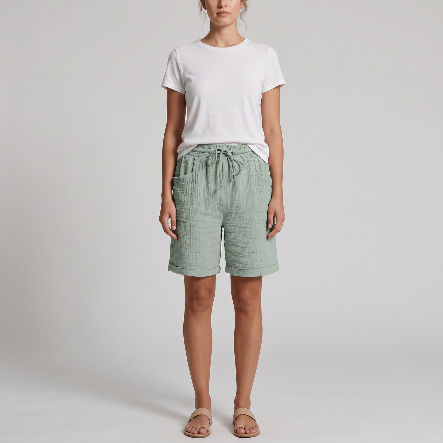 Woman wearing Josie sage green crinkle cotton bermuda shorts with a white tee, front view