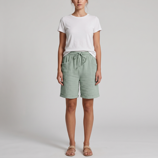Woman wearing Josie sage green crinkle cotton bermuda shorts with a white tee, front view
