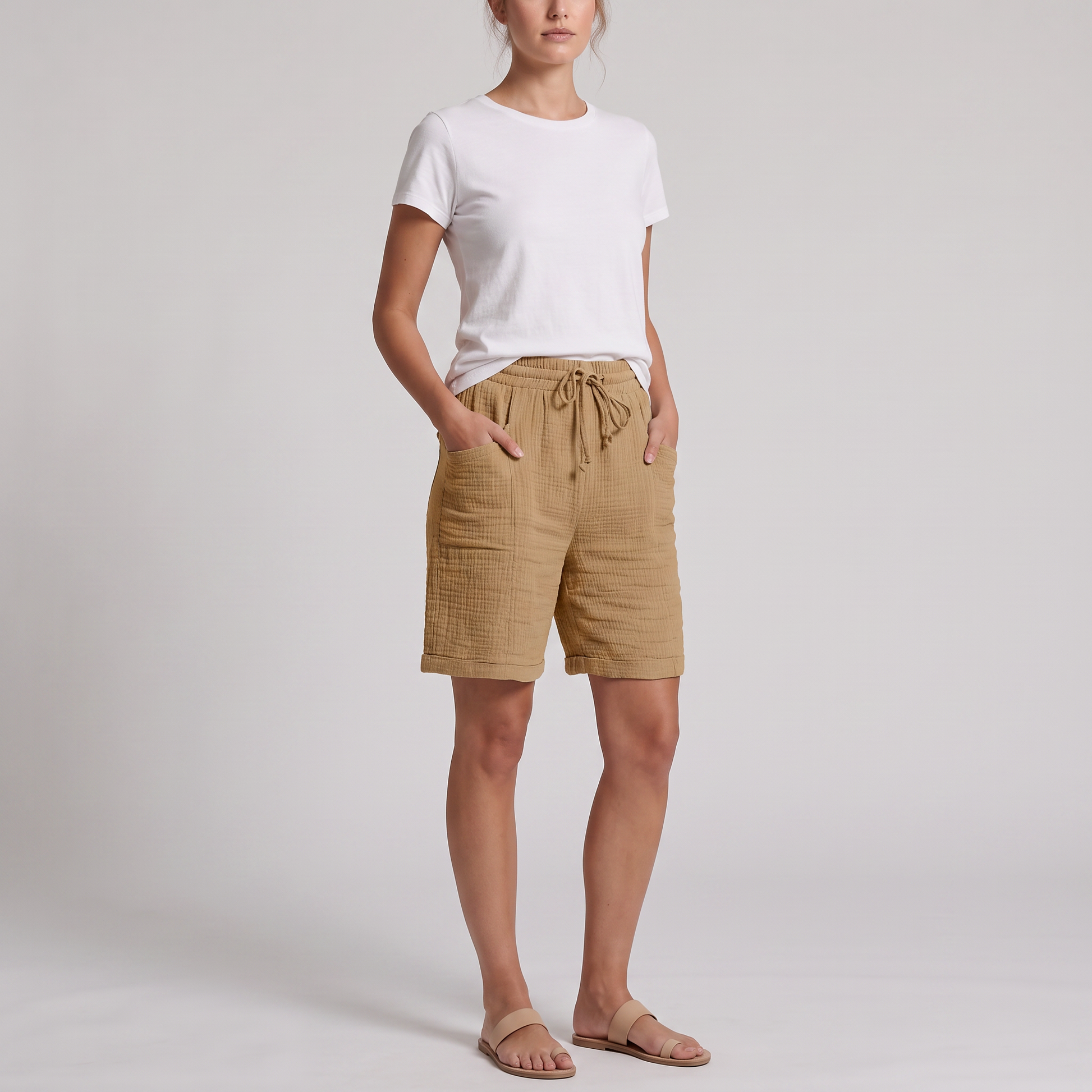 Woman wearing Josie tan crinkle cotton bermuda shorts with a white tee, hands in the side pockets
