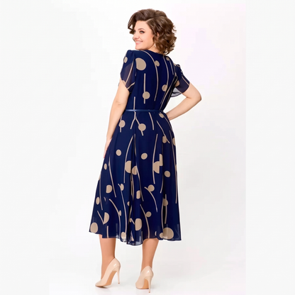 Back view of the Marjorie navy polka dot chiffon midi dress showing the flared pleated skirt and belted waist