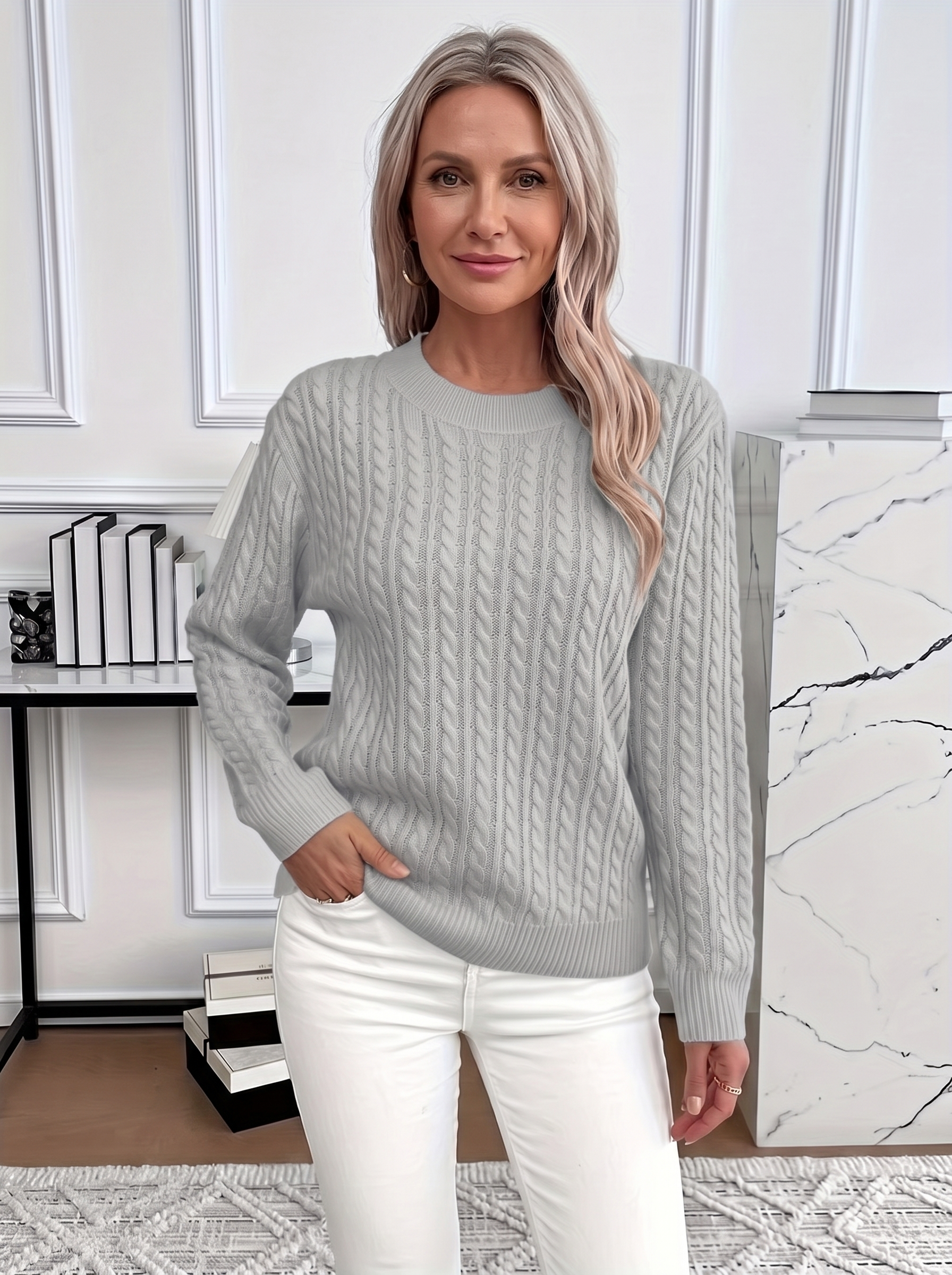 Woman wearing the Evelyn cozy cable knit sweater in light gray with white trousers