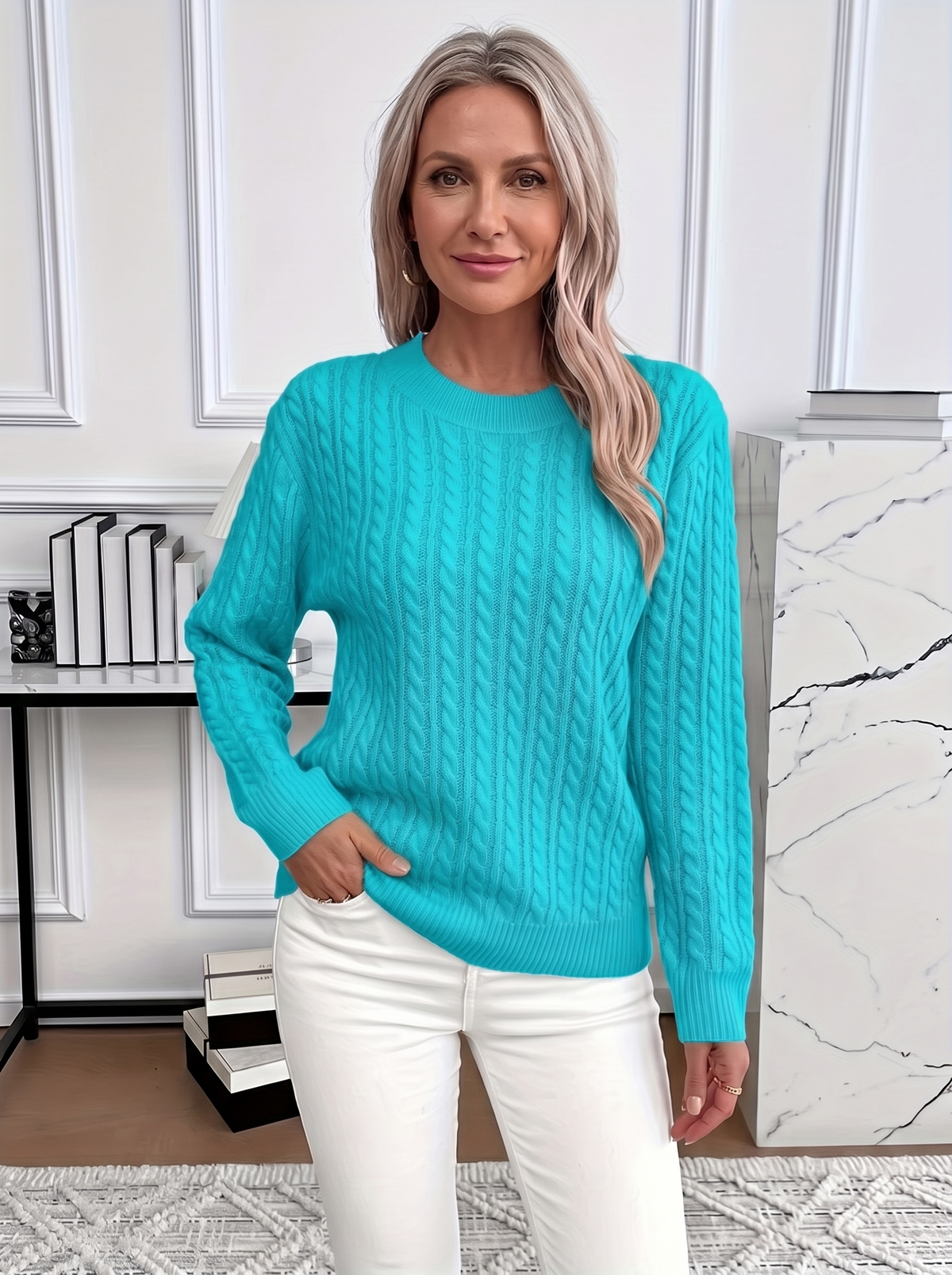 Woman wearing the Evelyn cozy cable knit sweater in turquoise with white trousers