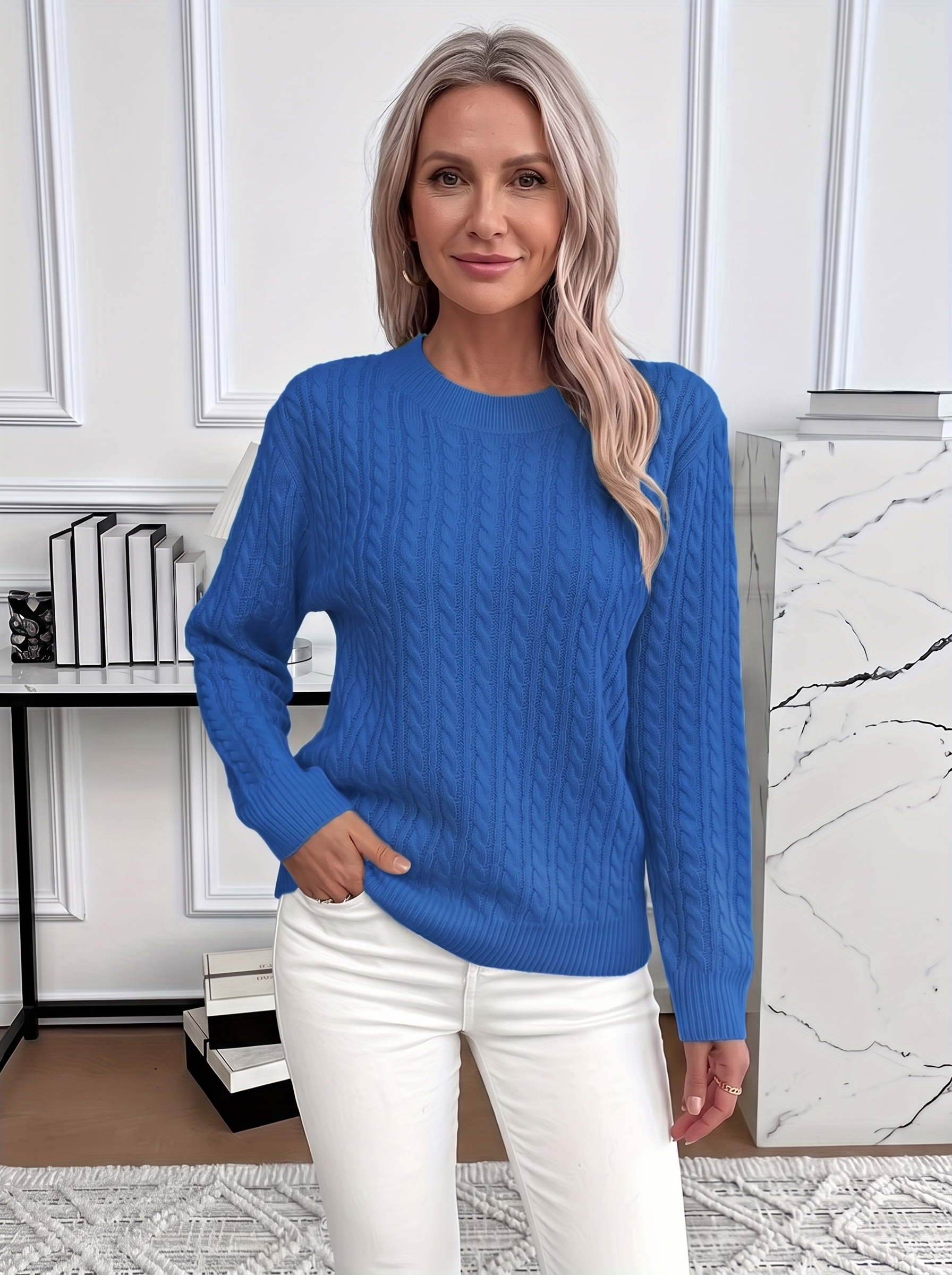 Woman wearing the Evelyn cozy cable knit sweater in royal blue with white trousers
